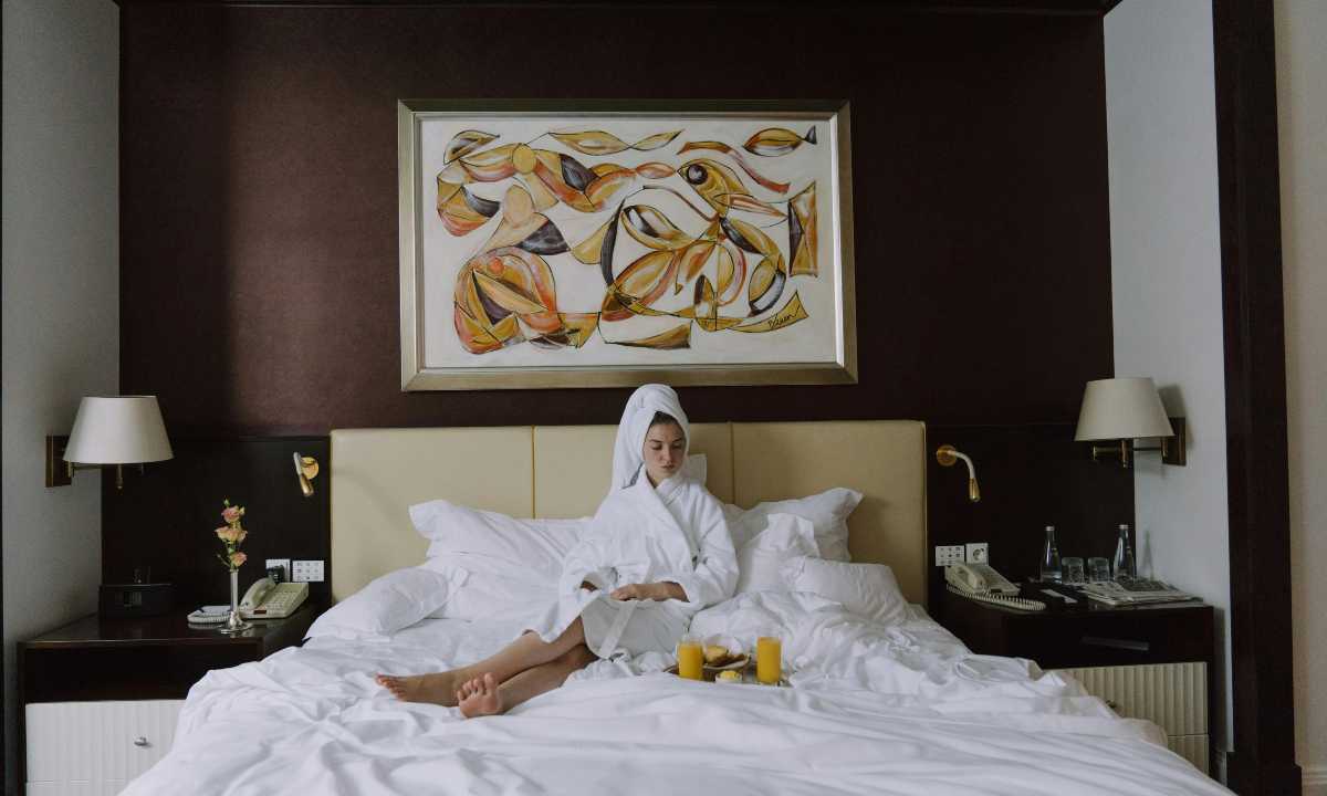 Donna su letto di hotel in accappatoio con colazione