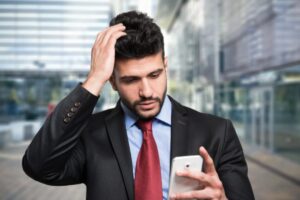 uomo preoccupato che guarda il cellulare e con una mano in testa