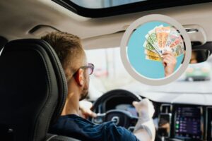 uomo alla guida di un'auto e nel riquadro una persona con delle banconote in mano