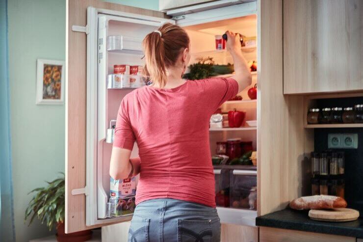 Donna prende qualcosa dal frigorifero aperto