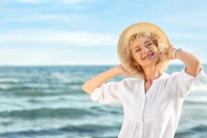donna anziana sorridente al mare con in testa un cappello