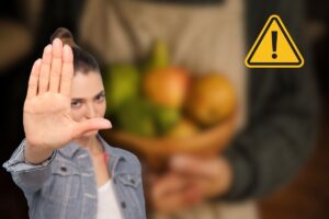 donna che tiene frutta in vassoio, altra donna che dice stop con le mani e segnale di pericolo