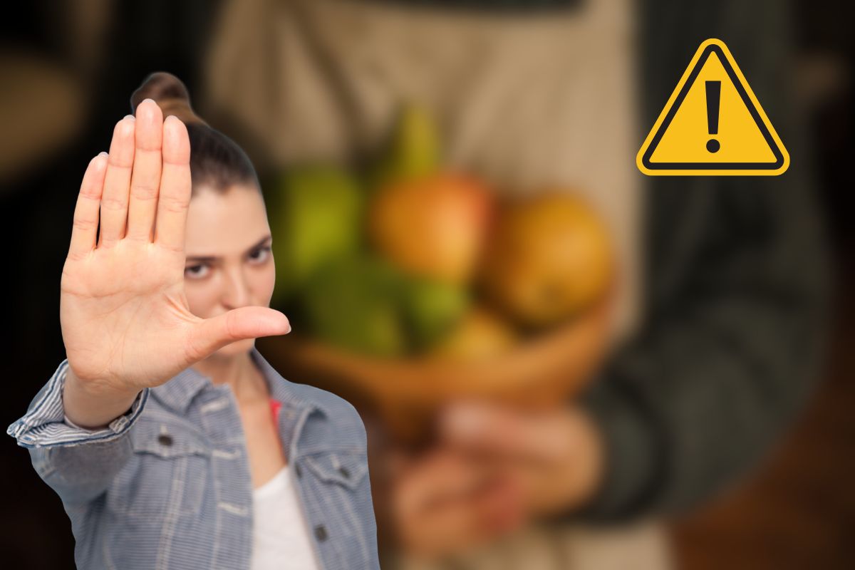 donna che tiene frutta in vassoio, altra donna che dice stop con le mani e segnale di pericolo