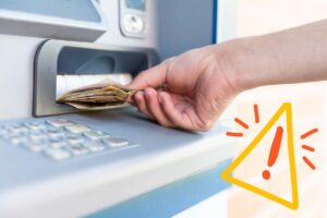 Persona che sta prelevando al bancomat ed un segnale di pericolo in basso a destra
