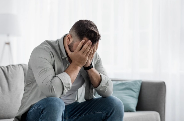 uomo disperato seduto sul divano con le mani in faccia