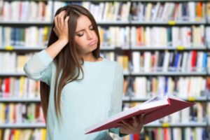donna che sbuffa mentre legge un libro con una mano sui capelli