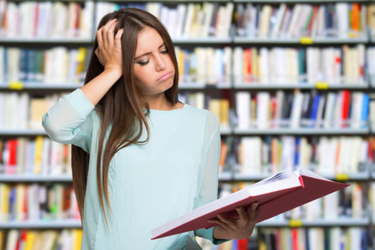 donna che sbuffa mentre legge un libro con una mano sui capelli