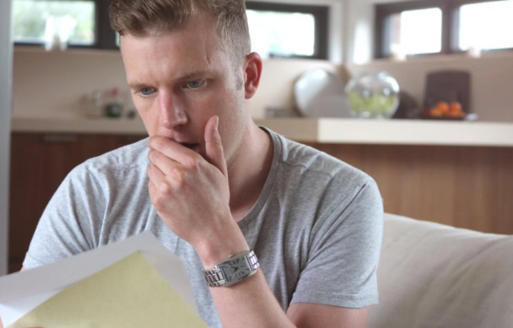 uomo preoccupato con una mano sulla bocca mentre legge un foglio