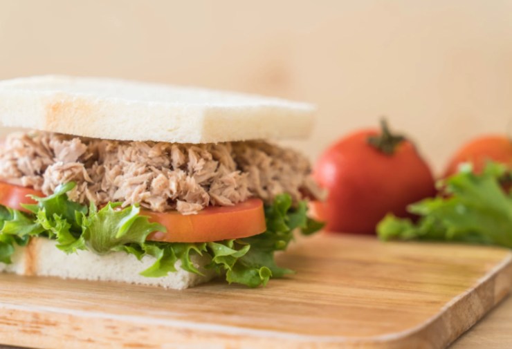 tramezzino farcito con tonno, insalata e pomodori sopra ad un tagliere di legno
